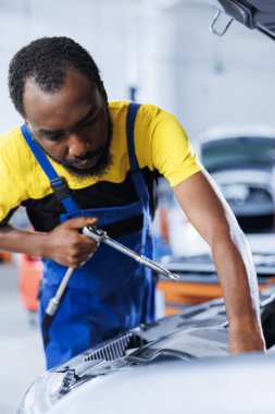 Araba servisindeki Afrikalı Amerikalı tamirci bozuk motoru değiştirdikten sonra vidaları sıkmak için tork anahtarı kullanıyor. Yetenekli garaj çalışanı, arızalı müşteri otomobilini tamir etmek için profesyonel araçlar kullanıyor