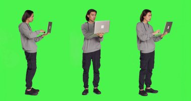 Modern adam dizüstü bilgisayarda internet sayfasında geziniyor, tüm yeşil ekran arkaplanı üzerinde duruyor, kablosuz bilgisayar kullanarak online web sitesine göz atıyor. Sosyal medya sayfasını kontrol eden genç adam iş üzerinde çalışıyor.