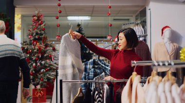 Bir kadın Noel için kıyafet mağazasında kıyafet karıştırıyor. Yeni yıl partisi için mükemmel kıyafetler arıyor. Moda mağazasının müşterisi ideal kıyafet arıyor.