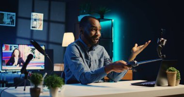 BIPOC içerik yaratıcısı selfie çubuğu akıllı telefonu kullanıyor, hayranları için yeni stüdyo tasarımını gösteren bir video hazırlıyor. Medya yıldızı kendini izleyiciler için cep telefonu kamerası ve el kamerasıyla çekiyor.