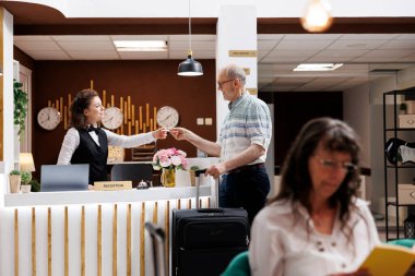 Kafkasyalı yaşlı adam otel lobisinin ön masasında kayıt yaptıktan sonra oda anahtarını kadın kapıcıdan alır. Yaşlı erkek turist, lüks kayıt gişesinde kayıt işlemini tamamladı.