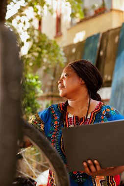 Sağlıklı, kendini adamış Afrikalı Amerikalı kadın bilgisayarını bozuk modern bisikleti tamir etmek için kullanıyor. Aktif kadın motosikletçi yaz tatilinde bisiklet bileşenlerinin güvenliğini artırıyor..