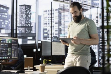 Programcı, büyük miktarda veriyi işleyebilen ve analiz edebilen karmaşık makine öğrenme modelleri yarattıktan sonra tablet üzerindeki sonuçları kontrol ediyor. Ofiste duran adam dijital cihaza bakıyor.