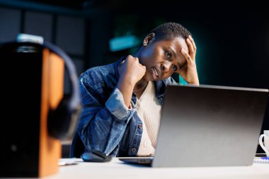 African American female freelancer looking stressed and frustrated as she uses her laptop. Black woman working at home appears tired and exhausted with headache while she browses on personal computer. clipart