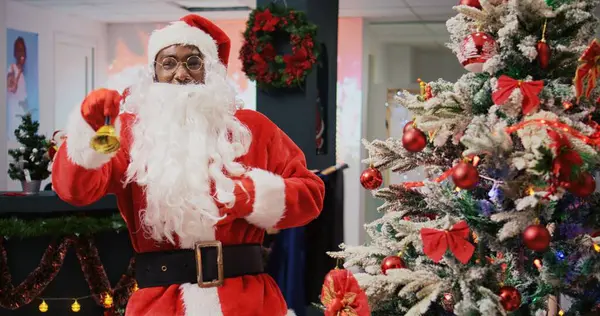 stock image Dolly in shot of merry manager dressed as Santa Claus in Christmas adorn shopping mall clothing shop. Supervisor jingling xmas bells and greeting customers in holiday themed fashion store