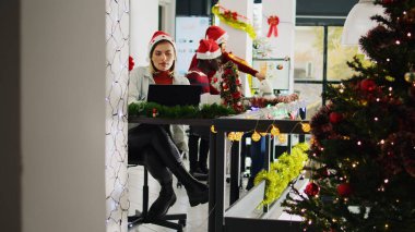 Noel 'de dekoratif bir ofiste çalışırken çalışanın kahvesini yudumlarken görüntüyü büyüt. Noel Baba şapkası takan personel çok ırklı çalışma alanında xmas süsleriyle süslenmiş.