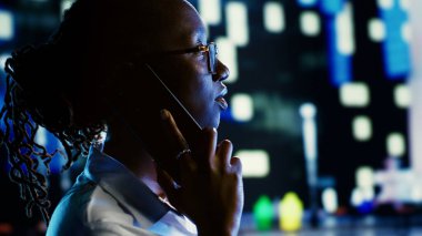 Kocasıyla telefonda konuşan Afro-Amerikalı bir kadın akıllı telefon kullanarak kendini daha güvende hissediyor geceleri loş bir şekilde aydınlanmış boş sokaklarda yürüyor, yakın çekim yapıyor, bulanık şehir geçmişi var.