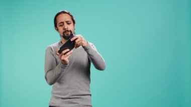 Akıllı telefonda video oyunları oynayan memnun bir adam, online ve stüdyo arkaplanlarında rakiplerine karşı zafer kazandıktan sonra kutlama yapıyor. Oyuncu cep telefonuyla B kamerasıyla oyunu kazanmaktan heyecan duyuyor.