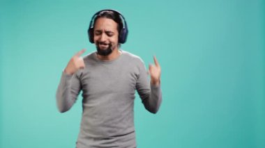 Mutlu insan eğleniyor, ritimle dans ediyor, kulaklıkla müzik dinliyor, boş zamanların tadını çıkarıyor. Neşeli adam şarkılar üzerinde eğlenceli hareketler yapıyor, stüdyo arka planında izole edilmiş, kamera B