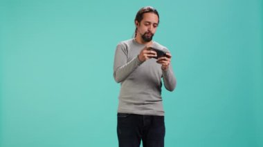 Akıllı telefondan tek kişilik video oyunu oynayan adam hobisinden zevk alıyor. Oyuncu telefondaki interaktif oyundan zevk alıyor, eğleniyor, stüdyo arka planında izole edilmiş, kamera A