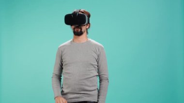 Sanal gerçeklik kulaklığı takan, arayüzle etkileşim kuran, hareketler yapan bir adam. İleri teknoloji modern VR aygıtı kullanarak eğlenen kişi, mavi stüdyo arka planında izole edilmiş, kamera B