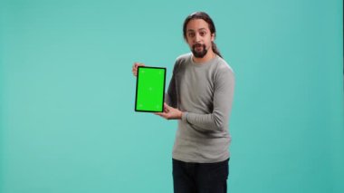Neşeli adam yeşil ekran tabletinde video sunuyor, stüdyo arka planında izole edilmiş. Boş fotokopi alanı kroma anahtar aygıtı kullanan neşeli kişi, kamera A