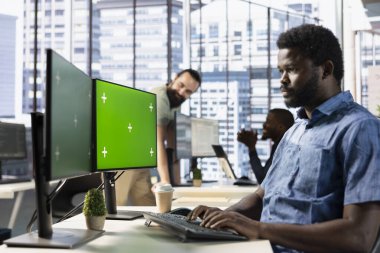 Yeşil ekran bilgisayarı üzerindeki veri tabanlarını analiz eden, pazarlama grafiklerini karşılaştıran ve muhasebe rakamlarını kontrol eden odaklanmış bir çalışan. Model PC 'deki takım projesi için görevleri çözen Afrikalı Amerikalı işçiler