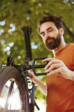 Canlı, beyaz erkek, bisiklet parçalarını ev bahçesinden profesyonel iş aletleriyle tamir ediyor. Aktif hevesli adam dışarıda bisiklet kolu ve pedalı tamir ediyor..