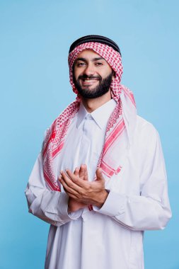 Geleneksel kıyafetler giyen Müslüman bir adam stüdyoda elleri ile alkışlayarak destek jesti yapıyor. Gülümseyen Arap kollarını çırpıyor ve heyecanlı bir ifadeyle kameraya bakıyor.
