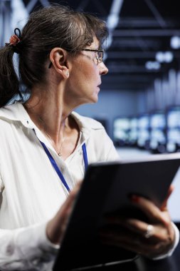 Old computer scientist updating data center rackmounts, writing intricate binary code scripts on tablet, using programming to fortify cybersecurity in technically advanced supercomputer hub clipart