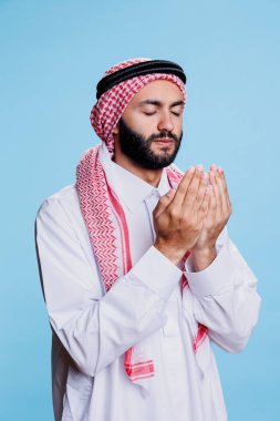 Geleneksel başörtüsü takan ve Tanrı 'ya kapalı gözlerle dua eden Müslümanlar. Arap adam ghutra başlık ve bornoz giymiş. Tanrı 'dan kutsamasını isterken açık plaklarla poz veriyor.