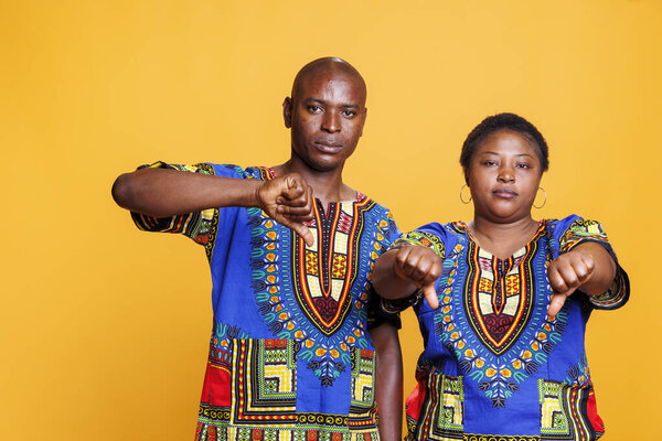 Man and woman standing with thumbs down gesture and looking at camera with serious expression. Confident mid adult black couple showing dislike and disagreement sign portrait