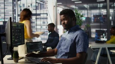 Adam bilgisayar ekranında evrak işlerini kontrol ediyor, görevleri çözüyor. Belgelerin kalite güvencesi beklentilerine ve standartlarına uygun olduğundan emin olmak için Afrika kökenli Amerikalı muhasebeci, kamera B