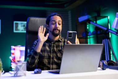Genç adam cep telefonuyla ailesiyle yaptığı konferans görüşmesinde selam veriyor. Erkek üniversite öğrencisi, akıllı telefon aracılığıyla iş arkadaşlarıyla görüntülü konuşma yapıyor..