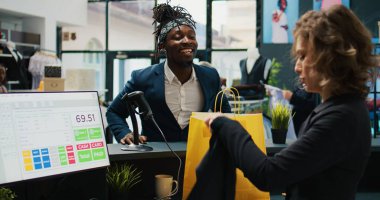 Perakende satış elemanı, müşteriler için giysileri bir kese kağıdına koyar, yazar kasada çalışır ve mağazada resmi moda ürünleri satar. Kadın çalışan, Afrikalı Amerikalı müşteriye yardım ediyor. Kamera B.