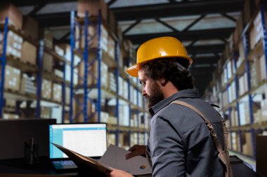 Depot worker examining products orders on laptop and reading dispatch notes before approving stock delivery. Industrial manager working on supply chain merchandise and shipment. clipart