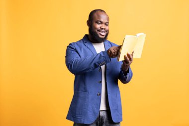 Yayımcıdan yeni çıkmış bir ciltli kitap okuyan adam ilgi çekici bir hikayeyle eğleniyor. BIPOC çalışanı stüdyo arka planında boş zamanlarında edebiyat romanının keyfini çıkarıyor