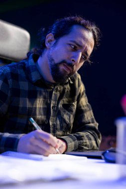 Not defterine erkek blogcu yazısının detaylı görüntüsü, blogu için içeriği gözden geçirip planlama. Sakallı adam dizüstü bilgisayarına bakarken not defterini kullanıyor..