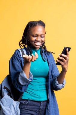 Telekonferans toplantısında arkadaşlarıyla komik sohbetler yapan mutlu bir kadın. Akıllı telefon, stüdyo geçmişi. BIPOC genç kızı çevrimiçi video görüşmesi sırasında arkadaşlarıyla takılırken eğleniyor