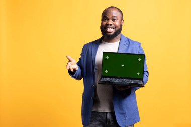 Yeşil ekranlı dizüstü bilgisayardan bahseden ve övgüler yağdıran göz alıcı bir adamın portresi. Canlı kişi sunar. Model defteri, olumlu değerlendirme, stüdyo arka planında izole edilmiş.