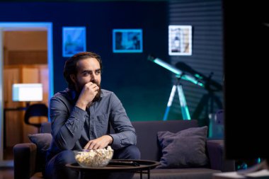 Kanepede patlamış mısır yiyen, iş gününden sonra oturma odasında aylak aylak oturup haber izleyen bir adam. Atıştırmalıkları seven ve yetişmek için TV kanallarına bakan biri.