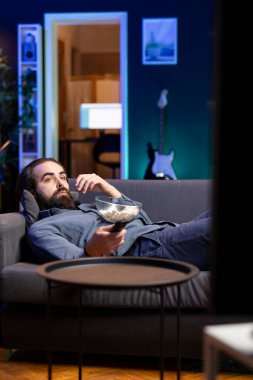 Ev sahibi evde sıkıldı, abonelik temelli yayın hizmetleri serisi için TV kullanıyor. Adam kanepede uzanmış, TV 'de VOD şovlarının keyfini çıkarıyor, patlamış mısır yiyor.