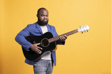 BIPOC çalışanı konser sırasında şarkı söylemeden önce gitar akort ediyor, stüdyo arka planında izole edilmiş. Sinirli sanatçı akustik akustik enstrüman ile akordu bozuk, tamir ediyor.