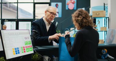 Alışveriş merkezindeki üst düzey müşterilere giysi satan çalışanlar, müşteriler için kese kağıdında kıyafet hazırlıyorlar. Yaşlı adam kasaya mal almak için yaklaşıyor. Kamera B.