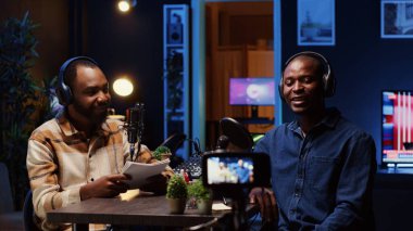 Internet show host making guest laugh, cracking jokes during comedy focused podcast. Talking show interviewer broadcasting live from living room studio decorated with neon lights clipart