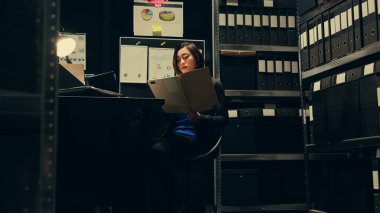 Polisin arşiv odasında çalışan özel bir ajan resmi kayıtları ya da dava soruşturmasıyla ilgili belgeleri okumak için. Dedektif memur şüphelilerin geçmişini araştırıyor. Kamera B.