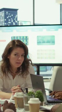 Dikey Video Finans uzmanı konferans odasındaki belgelerle ilgili istatistik verilerini gösteriyor, sunum için personelle brifing veriyor. Pazar ihtiyaçlarına uyum sağlamak için satış raporlarını inceleyen iş arkadaşları