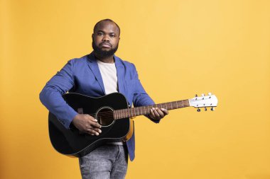 Akustik gitar telleriyle çalan Afro-Amerikan bir adamın portresi. Stüdyo arka planında izole bir şekilde hobisinden zevk alıyor. Müzik enstrümanında şarkı söyleyen yetenekli bir müzisyen.