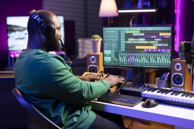 Genç söz yazarı amfi tuşlarını çeviriyor ve sesleri bir konsolla karıştırıyor, dijital bir yazılımda kayıt ayarlarına bakıyor. Sanatçı müzisyen yeni yeni parçalar yapıyor, müzik setleri ev stüdyosunda..