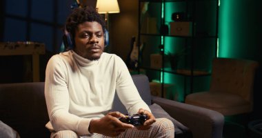 Neon ışıklı oturma odasında kanepede oturan adam oyun konsolunda video oyunları oynayarak rahatlıyor. Çevrimiçi çok oyunculu turnuvada yarışarak oyuncuların dairede dağılmasına yakınlaştır