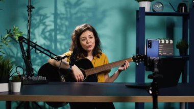 Gitar tutan sanatçı, aboneler için çevrimiçi konser sırasında şarkı söylemek için heyecanlı. Sosyal medyada canlı performans sırasında akustik müzik enstrümanında şarkı söyleyen kadın, kamera B