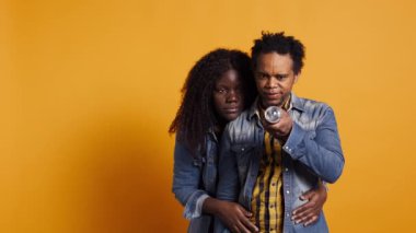 Afro-Amerikalı adam korkmuş karısını korumak için el fenerini kullanıyor. Korkan kadın sarı arka plandan korunmak için sevgilisinin arkasına saklanıyor. Korkmuş bir an. Kamera B.