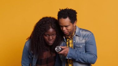 Stüdyoda kocasının arkasına saklanan korkmuş kadın, fenerli bir şey arayan ve ortağını koruyan adam. Tehlike kaynağı arayan korkmuş bir çift. Kamera A.