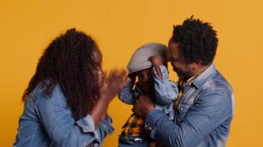 Sarı arka planda birlikte poz veren Afro-Amerikan neşeli bir aile, mutlu bir çift küçük çocuklarına sarılıyor. Gülümseyen anne ve baba çocuklarına sevgi gösteriyorlar. Kamera A.