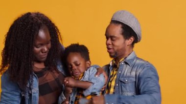 Genç bir aile, sarı arka planda oğluyla birlikte akıllı telefondan selfie çektirmek için gülümsüyor ve tatlı anılarını yakalıyorlar. Gururlu Afrikalı Amerikalı anne ve baba çocukla poz veriyor. Kamera A.