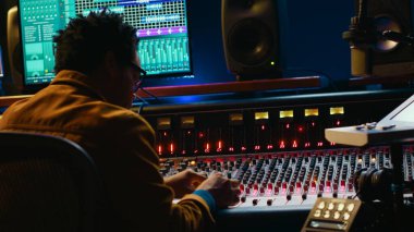 Afrika kökenli Amerikalı ses mühendisi ses karıştırma konsolunu kullanarak şarkıları yönetir, müzik sonrası prodüksiyon yapar. Yapımcı motorlu kontrol düğmelerine basıyor, kurgu yazılımına bakıyor. Kamera A.