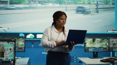 Afrika kökenli Amerikalı menajer ekibine şehirdeki trafik akışını gözlemleyerek büyük ekrandaki güvenlik görüntülerini izlemeleri için rehberlik ediyor. Devlet dairesi CCTV uydu sistemini çalıştırıyor. Kamera B.