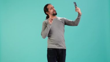 Akıllı telefonu kullanarak selfie çeken ve sosyal medyaya, stüdyo arkaplanına koyan bir adam. Fotograf makinesiyle fotoğraf çeken kibirli biri, stüdyo arka planında izole edilmiş, kamera A
