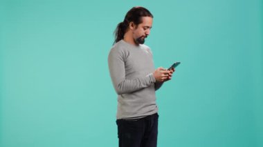 Mutlu adam en iyi arkadaşına akıllı telefon kullanarak mesaj atıyor, mesajlar okuyor. Rahat bir insan cep telefonuyla arkadaşıyla sohbet ederken eğleniyor, mavi stüdyo arka planında izole edilmiş, kamera A