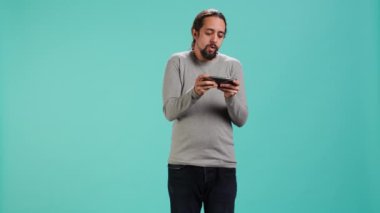 Odaklanmış adam cep telefonuyla yoğun video oyunu oynuyor, dokunmatik ekrandaki saldırı tuşlarını spamlıyor. Oyun yarışmasına katılan oyuncu, stüdyo arka planında izole edilmiş, kamera A